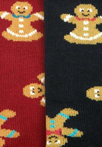 Calcetines rojos y negros con patrones de hombre de jengibre de punto, que presentan botones blancos y acentos en azul o rojo en las figuras.
