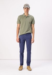 Polo de culoare khaki cu mâneci scurte, pantaloni bleumarin și adidași de culoare bej deschis. Ținuta este completată cu o șapcă gri.