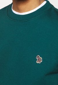 Sweatshirt en teal à col blanc, avec un logo de cheval brodé multicolore sur la poitrine, fabriqué dans un matériau doux.