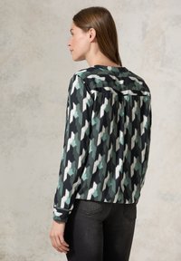 Blusa a maniche lunghe nera, verde e bianca con motivo, dotata di una piega posteriore. Texture liscia e vestibilità comoda.