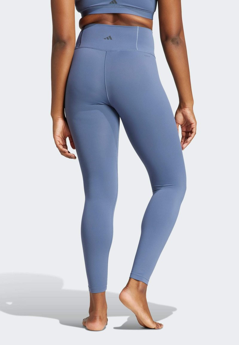 Lichtblauwe leggings, hoog in de taille, gemaakt van gladde stof met subtiele naden, blote voeten en merken in de buurt van de taille.
