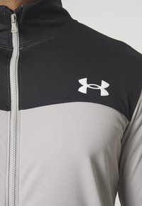 Gros plan d'une veste zippée noire et grise avec un logo blanc Under Armour sur la poitrine.