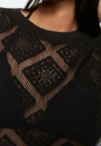 Black knit sweater featuring a diamond mesh pattern with open weave. Rounded neckline, long sleeves, and textured fabric.