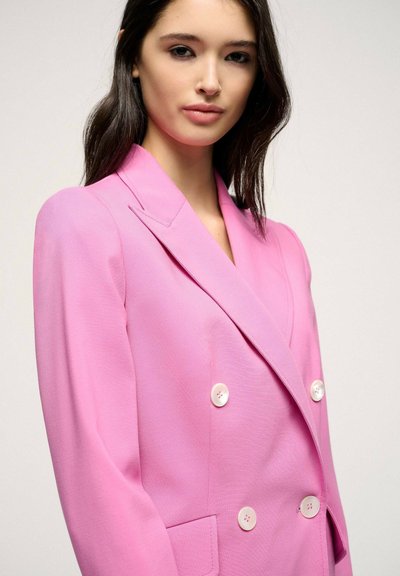 Double-breasted pink blazer with notched lapels, two front pockets, and white buttons. Smooth texture and tailored fit.