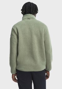 Flísová bunda v tlmenej zelenej farbe s textúrovaným, nadýchaným povrchom. Má vysoký golier a dlhé rukávy, navrhnutá pre teplo a pohodlie.