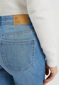 Světle modré džíny z denimu s vynikající koženou ná šivkou označenou "BLUE RIDGE". Tkanina vypadá jemně, s jemnou texturou a detaily šití.