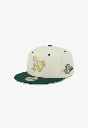 Gorra blanca con visera verde, con "A's" bordados en gris y dorado, y un parche metálico de un personaje de caricatura en el lateral.