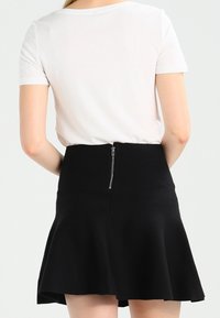 Svart utsvängd kjol med en strukturerad yta, utrustad med en silverdragkedja baktill och en åtsittande midja. Kombinerad med en vanlig vit T-shirt.