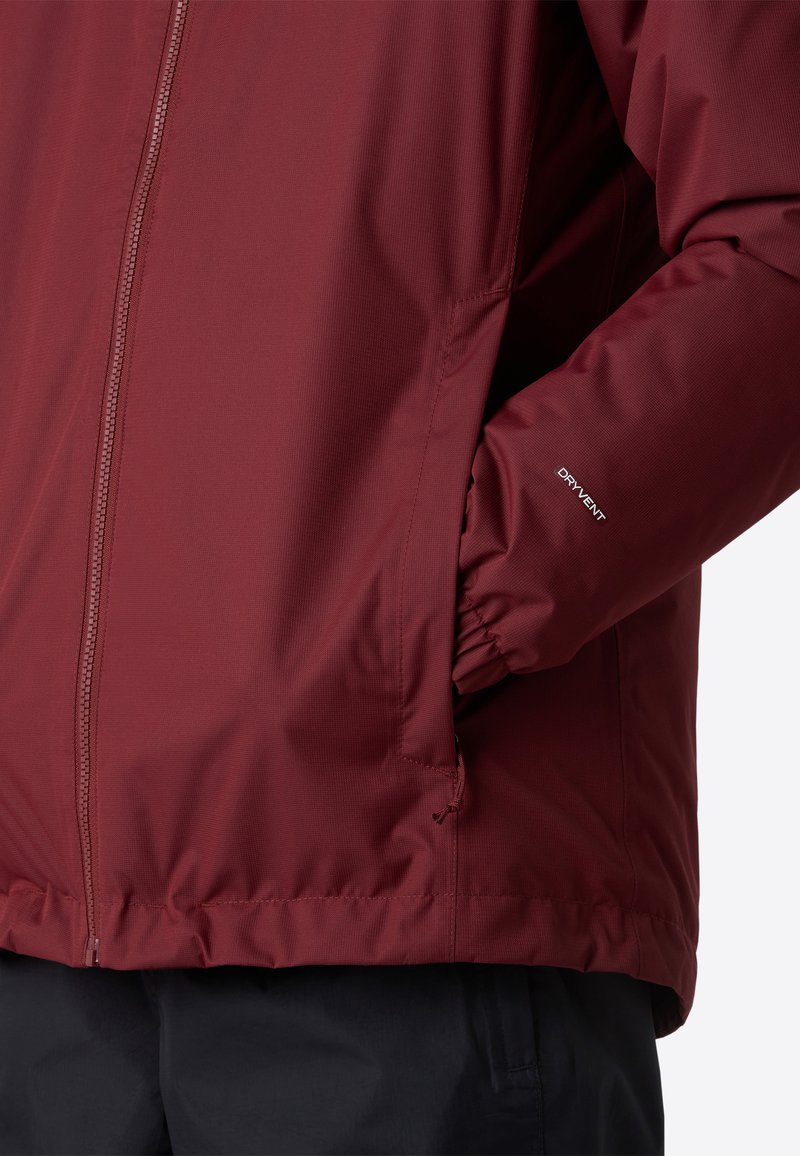 Giacca isolante color bordeaux con zip integrale, polsini elastici e tasche laterali. Presenta il marchio "DRY VENT" sulla manica. Texture liscia.