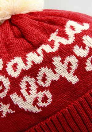 Beanie rosso lavorato a maglia con testo bianco. Parte superiore decorata con un soffice pom-pom color crema. Il testo appare in un font giocoso e corsivo.
