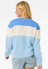 Sudadera color bloqueada en azul y gris claro con cuello redondo y corte relajado. Presenta puños y dobladillo de canalé, y su textura es suave.