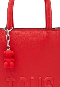 Bolso de mano de cuero rojo con acabado texturizado, que presenta una cadena de sierra plateada y un charm de oso de goma roja adjunto a la cremallera. Detallado con un logo en relieve.