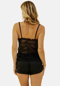 Débardeur en dentelle noire avec des bretelles ajustables et un motif floral, associé à un short en satin noir avec une texture lisse et un ourlet arrondi.