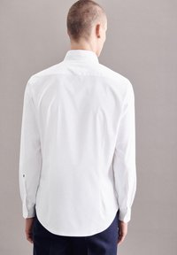 Camicia bianca a maniche lunghe con colletto button-down, orlo curvo e polsini a doppio bottone. Tessuto liscio con cuciture minime e senza motivi visibili.