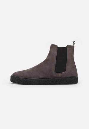 Bottine en daim gris foncé avec panneau latéral élastique noir, semelle texturée noire et languette à tirer sur fond blanc.