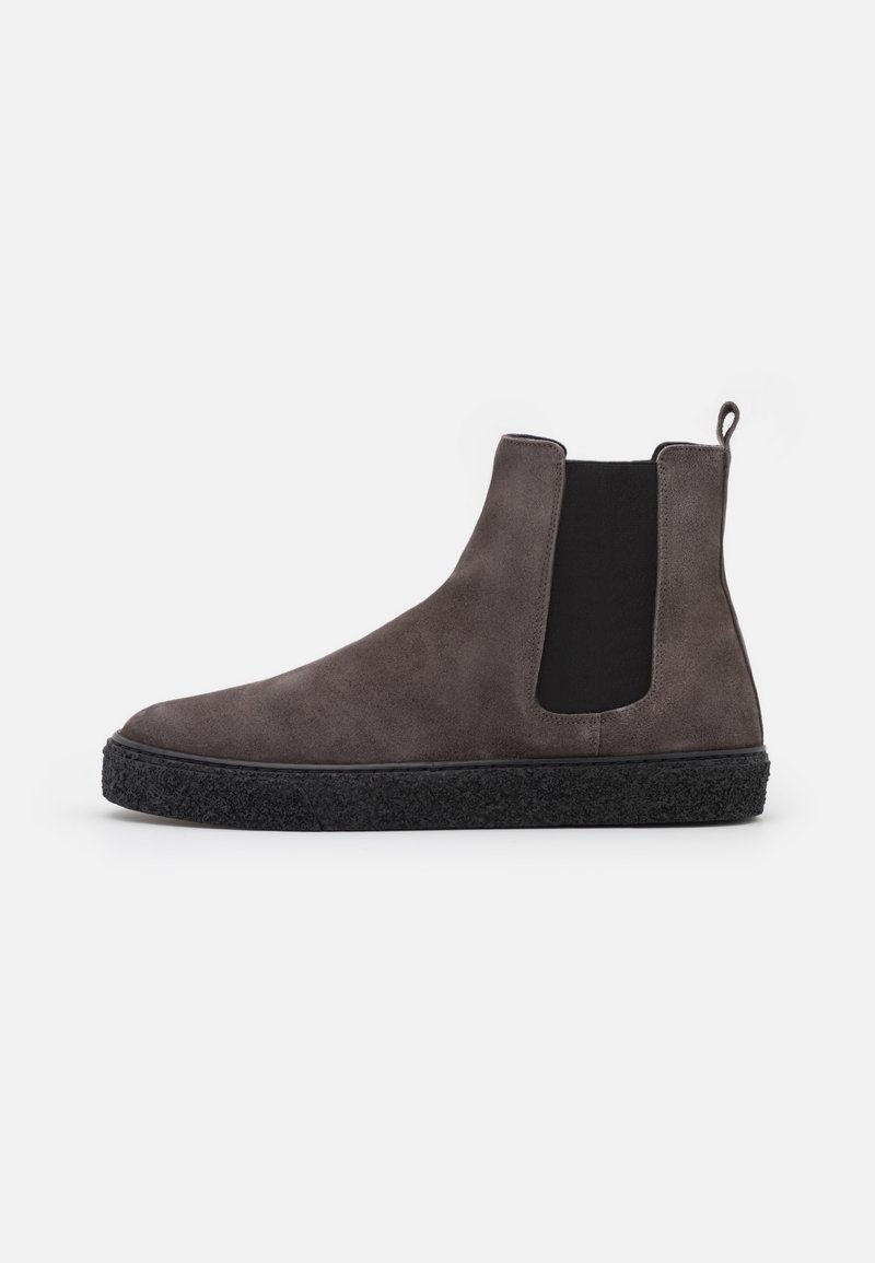 Bottine en daim gris foncé avec panneau latéral élastique noir, semelle texturée noire et languette à tirer sur fond blanc.
