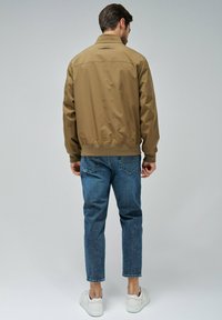 Veste bomber synthétique marron avec col montant, poignets et ourlet côtelés, associée à un jean en denim bleu et des baskets blanches.