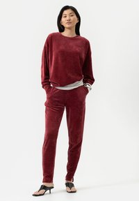 Carmijn fluwelen loungewearset met een losse lange mouwen top en bijpassende taps toelopende broeken, weergegeven met een gelaagde grijze top eronder.