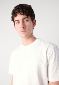 White cotton t-shirt with a round neckline and short sleeves. Subtle logo on the chest, smooth texture, and relaxed fit.