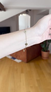 Goldene Kettenarmband mit runden Charms; ein Charm zeigt klare Steine, der andere ein strukturiertes Design. Glatte Textur und zartes Erscheinungsbild.