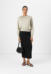 Helles beige Sweatshirt mit langen Ärmeln und gerafftem Saum, kombiniert mit einem schwarzen, figurbetonten Midirock, einer schwarzen Umhängetasche und schwarzen Riemchensandalen.