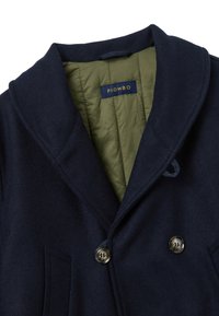 Abrigo de lana azul marino con diseño de doble botonadura, solapas con muesca y dos botones en tono dorado. Forrado con tejido acolchado verde.