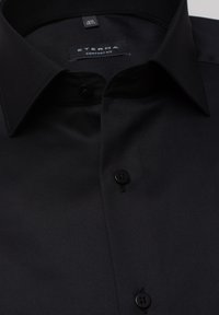 Schwarzes Eterna Hemd im Comfort Fit mit glatter Textur, klassischem Kragen und schwarzen Knöpfen, das ein schlichtes und sauberes Design aufweist.