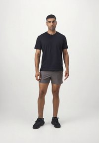 Fekete póló, szürke sport rövidnadrág és fekete tornacipő. Egyszerű kialakítás, rövid ujjú és kényelmes szabás. Sima anyag és minimális díszítés.