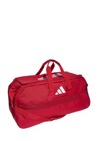 Borsa a duffel rossa realizzata in tessuto con base rinforzata, dotata di due manici superiori e una tracolla regolabile. Include logo e strisce bianche.