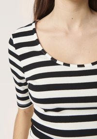 Top a righe bianco e nero con texture a costine, maniche corte e scollatura ampia. Le righe sono di uguale ampiezza, creando un motivo uniforme.