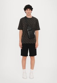 Cămașă scurtă cu mânecă, modelată negru, pantaloni scurți negri, adidași albi și o geantă neagră purtată pe umăr. Design minimalist, croială lejeră.