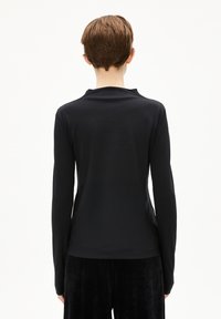 Schwarzes Langarmoberteil mit enganliegendem Design und weicher Textur, mit einem dezenten hohen Kragen und nahtlosen Schultern, kombiniert mit dunklen Hosen.