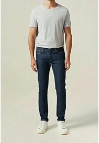 Camiseta gris de manga corta combinada con vaqueros denim azul oscuro y zapatillas blancas. Los vaqueros tienen un ajuste clásico y detalles de costuras sutiles.