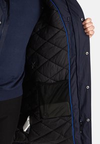 Giacca puffer blu navy con interno trapuntato nero, dotata di bordi azzurri, una tasca con zip e una tasca in rete interna.