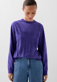 Lilla striktrøje med rund halsudskæring og struktureret chevronmønster på forsiden. Sammen med blå denimjeans.
