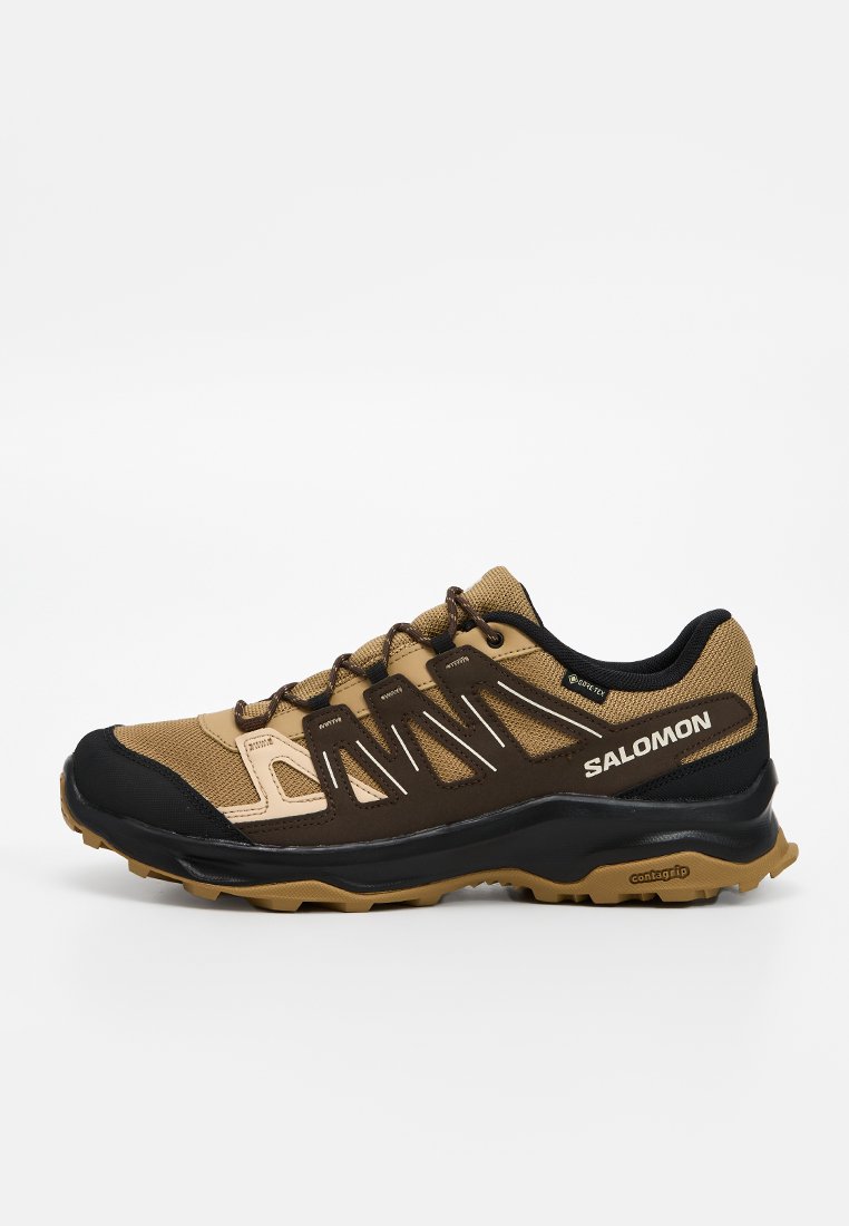 Zapatillas deportivas marrones y negras con parte superior de malla y sintético, diseño de cordones, suela texturizada y la marca "SALOMON" en el lateral.