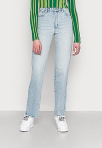 Jeans de perna reta azul claro com um acabamento desbotado, cintura alta e cinco bolsos, combinados com ténis brancos com um padrão floral.