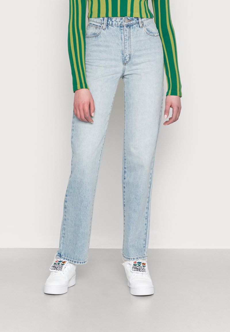 Jeans de perna reta azul claro com um acabamento desbotado, cintura alta e cinco bolsos, combinados com ténis brancos com um padrão floral.