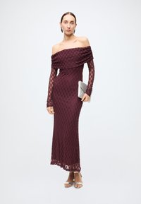 Burgundy lace evening dress with off-shoulder design and long sleeves, featuring a fitted silhouette and a scalloped hem. Silver clutch and heels.