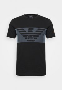 Svart bomullströja med en grå logotyp med vingar över bröstet, korta ärmar och rundad halsringning. Texturerade detaljer på sidorna.