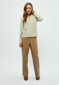 Beige Langarmshirt mit V-Ausschnitt und lässigem Schnitt, kombiniert mit hochgeschnittenen braunen Hosen. Glatte Stoffqualität und gerades Hosen-Design.