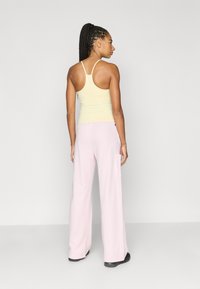 Ανοιχτό κίτρινο εφαρμοστό τοπ με λεπτές τιράντες συνδυασμένο με φαρδιά, ανοιχτό ροζ παντελόνια με πλαϊνές τσέπες.