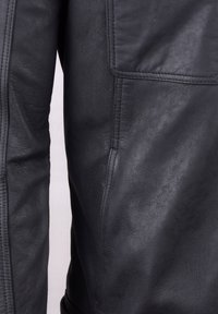 Black leather jacket featuring smooth texture, visible stitching, and a pocket detail on the left side.