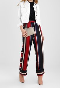 Giacca in denim bianco, top nero, pantaloni a vita alta a righe rosse e nere con accenti blu e beige, abbinati a una borsa grigia chiara e tacchi nude.