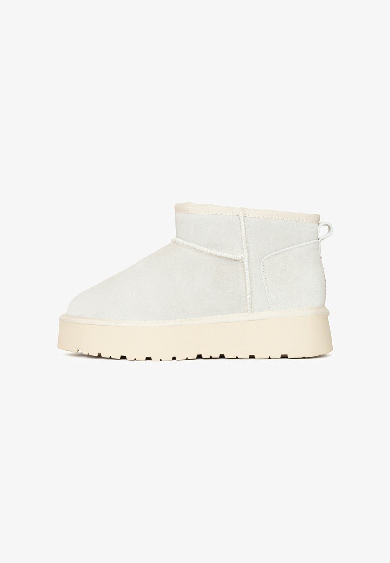 Witte suède enkellaars met een gestructureerd oppervlak, ronde neus en een dikke beige rubberen zool. Beschikt over een trekband aan de achterkant voor gemakkelijk aan- en uittrekken.