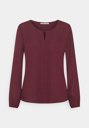 Blouse à manches longues pour femme en bordeaux profond avec encolure ronde, plis verticaux sur le devant et légère découpe en forme de goutte au niveau du col.