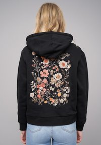 Felpa nera con un design floreale ricamato in colori pastello sulla schiena. Dotata di cappuccio con cordoncino e polsini e orlo a costine.