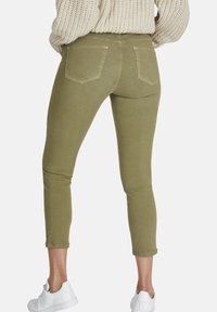 Jeans de mezclilla elástica en verde oliva con un diseño ajustado, puños enrollados y dos bolsillos traseros, combinados con zapatillas blancas.