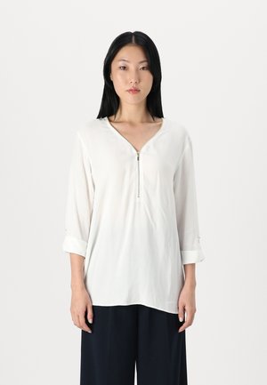 Witte blouse met een ritsdetail bij de hals, driekwart mouwen opgerold en een gladde, lichte stof. Eenvoudig en strak ontwerp.