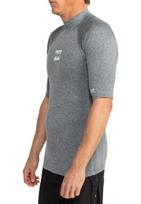 Rash guard gris de manga corta con cuello alto, hecho de un tejido elástico. Presenta un logotipo en el pecho y paneles texturizados en los hombros.